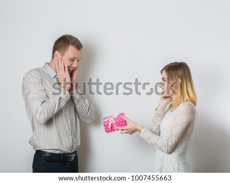 beautiful girl gives a gift to a guy, young couple, congratulates on a day all lovers, concept of a holy valentine, in a studio on a white background
