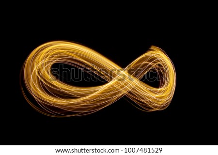 Gold light painting photography - infinity loop shape curves and waves of metallic yellow light against a black background