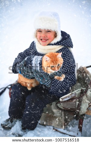 Little girl and a red cat on a sleigh ride in the countryside.