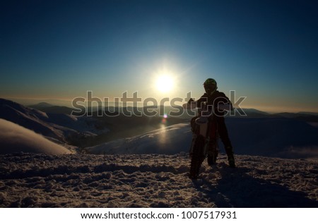 Extreme biker on sport motorcycle on winter snow mountain top on sunset sky background