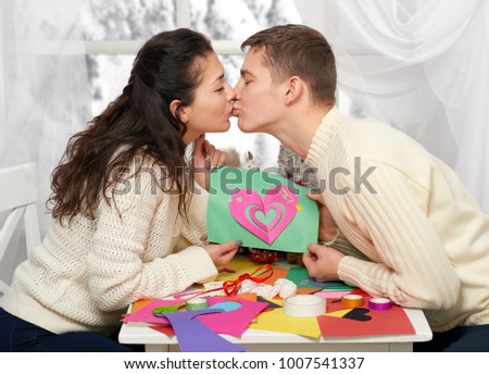 romantic young couple sit at the table and shows origami red heart, happy people and love concept