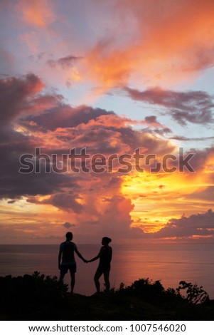 Two lovers on a romantic trip see off the sunset on the island of Bali. Orange, red sky. View from the mountain to the ocean