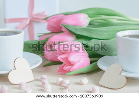 Romantic photo with pink tulips, two cups of coffee and wooden tiny hearts in the foreground