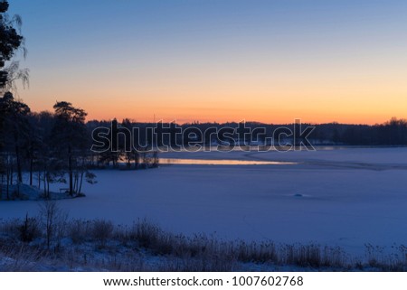 Beautiful nature and landscape photo of dusk winter evening in Katrineholm Sweden Scandinavia. Nice colorful outdoors image with blue and yellow colors. Calm, peaceful sunset at ice lake and forest.