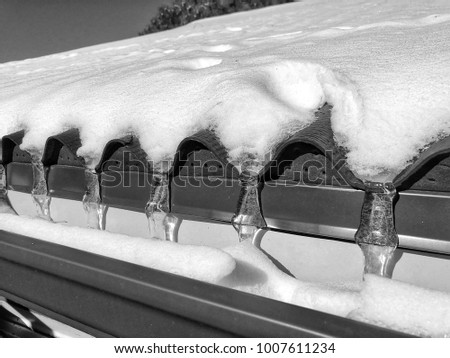 Shot of a corrugated style roof covered in snow. At each low point in the roofs design there is a small icicle. Black and white picture