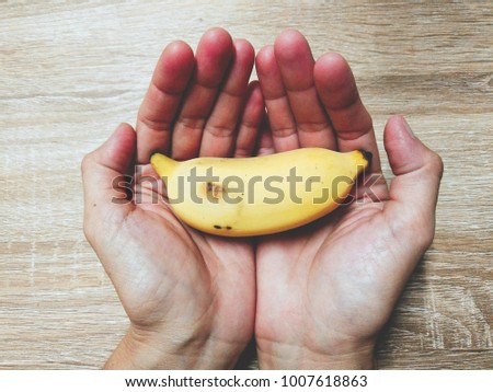 Yellow banana Placed in both hands on a brown wooden table.