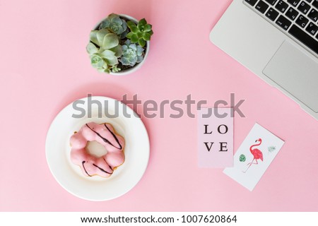on a pink paper background lie a laptop, a donut in pink glaze, cards with the inscription "Love" and flamingos, a flower succulent