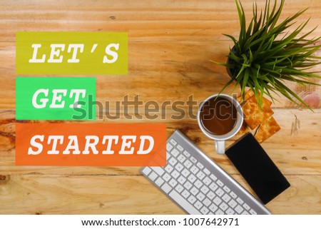 Keyboard,smartphone,notepad,pen,biscut,coffee and green plant on the wooden table. LET'S GET STARTED CONCEPT.