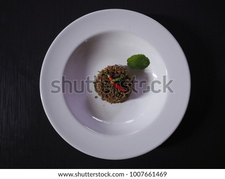 Top view picture of stir fried spicy ground beef on white plate above black texture.