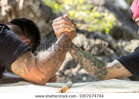 Two man with tattoo on arms engage in arm wrestling.
