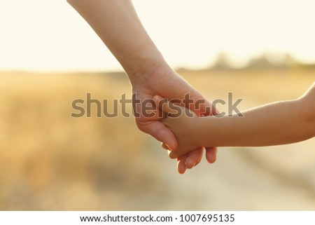 Father holds daughter by the hand. Shooting close-up. In the background, out of focus is a country road. Support on the way. Royalty-Free Stock Photo #1007695135