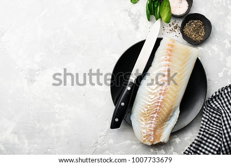 Fillet of fresh sea cod to prepare a healthy healthy dish with salt, ground pepper, fresh seasonal greens, lemon slices on the background with a kitchen knife for cutting. Copy space