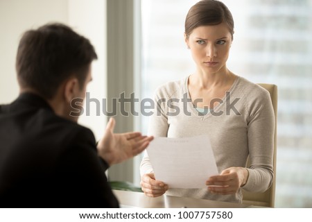 Millennial businesswoman with skeptical facial expression holding contract document and listening unconvincing offer of business partner. Suspicious terms of agreement, doubtful investor, fraud, scam Royalty-Free Stock Photo #1007757580