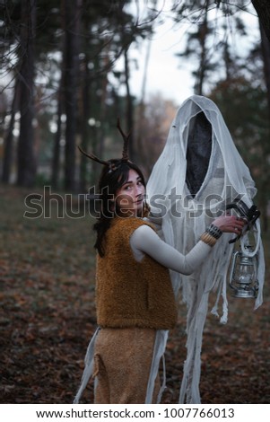 Girl in costume with horns faun  with a flashlight  in her hands posing in the autumn forest. Halloween, samhain