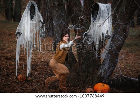 Girl in costume with horns walking among the ghosts in the autumn forest. Halloween, samhain