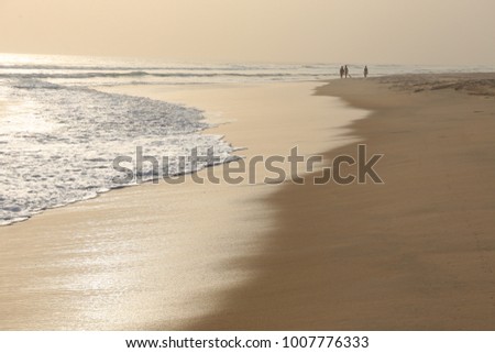 View of the beach near assinie in ivory coast. Sunset with people silhouettes at the horizon. White waves on the sand. Peaceful seascape in the evening. Happy picture taken on 29th december 2015.