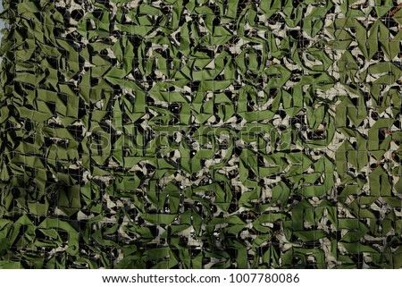 camouflage scrim in two layers, lit by sunlight with shade from the trees

