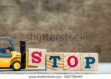 Yellow toy forklift hold letter block S to complete word stop on wood background