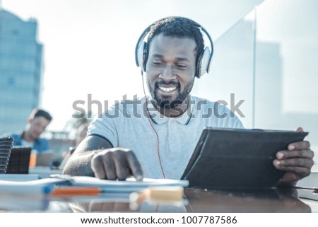 Education is the key to success. Low angle shot of a cheerful college guy smiling while enjoying the music playing in his headphones and working on a home assignment. Royalty-Free Stock Photo #1007787586