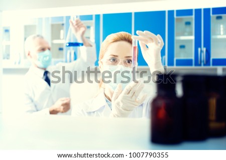 Let me see. Female scientist standing in a laboratory and holding a test tube with chemical liquid while analyzing it.