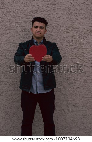 Latin guy leaning on a concrete wall giving his heart 