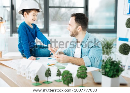 Advice needed. Charming young architect showing a color chart to his little son in a white hard hat and asking him to choose a color Royalty-Free Stock Photo #1007797030