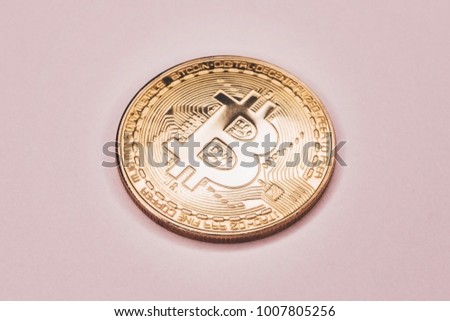 A large gold coin of crypto-currency bitcoin on a gentle pink background.