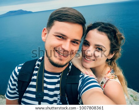 happy smiling couple travelers taking a selfie on the phone to rest against the sea