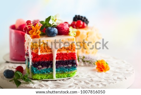 Various slices of cakes on a white tray: rainbow cake, raspberry cake and almond cake. Sweets decorated with fresh berries and flowers for holiday Royalty-Free Stock Photo #1007816050