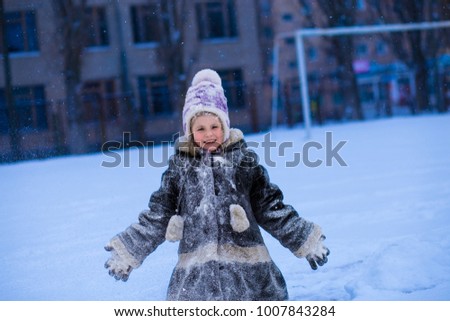 A cute little girl covered with snow has fun in winter park, wintertime