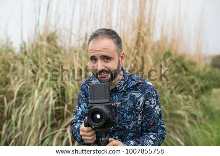Cheerful adult man with camera on background of grass.