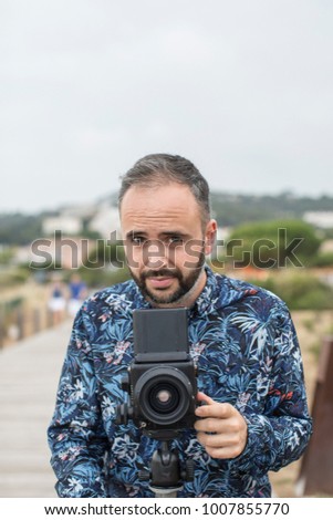 Adult bearded man standing and setting camera in cloudy day.