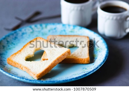 A  wheat toast with a hole in the shape of a heart in the middle on a blue  plate. Soft focus.
