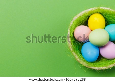 Six colorful pastel monophonic painted Easter eggs in basket with green grass isolated on green background. Happy Easter concept. Copy space for advertisement. With place for text. Top view on eggs
