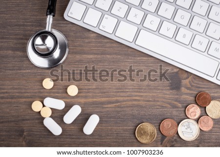 stethoscope, money and pills at the computer keyboard on a wooden table. health care and technology background