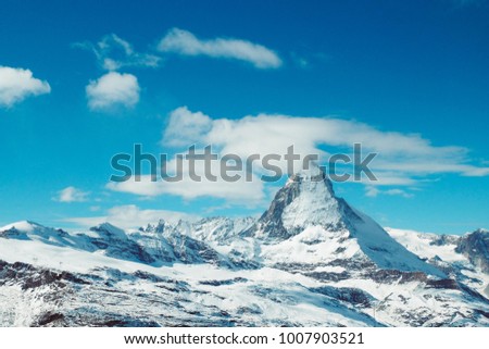 Matterhorn peak in sunny day with blue sky, snow and some clouds in background, Switzerland.