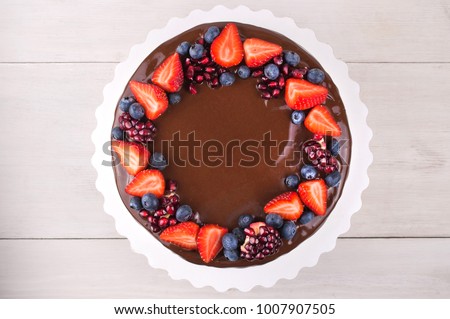 Birthday cake in chocolate with strawberries, blueberries and garnet on white wooden table. Top view. Picture for a menu or a confectionery catalog.
