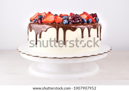 Birthday cake in chocolate with strawberries, blueberries and garnet on white wooden table. Picture for a menu or a confectionery catalog.