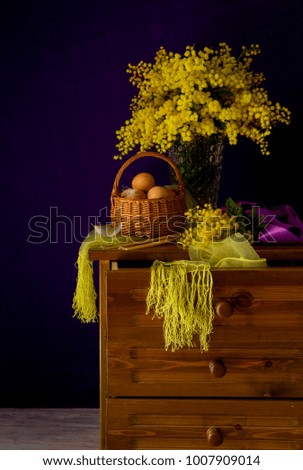 The easter still life. Eggs in a wicker basket, a bouquet of mimosa and church candles on wooden nightstand close-up.