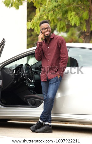 Full length portrait of handsome black man talking on mobile phone by car