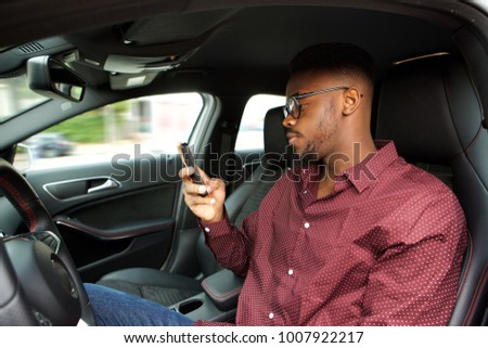 Portrait of young african american man looking at cellphone before driving in car
