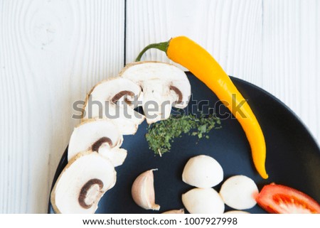 Preparing Food Concept. Ingredients for a meal: tomato, chili pepper,garlic,champignone mushroom, mozarella, herbs and spices on a black plate, white wooden background, top view