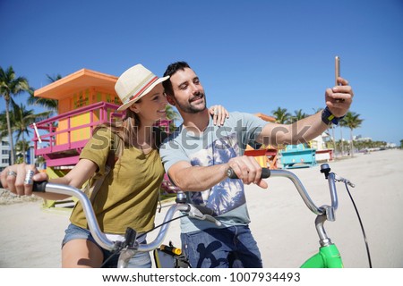 Young couple riding bikes in Miami beach, taking selfie pictures 
