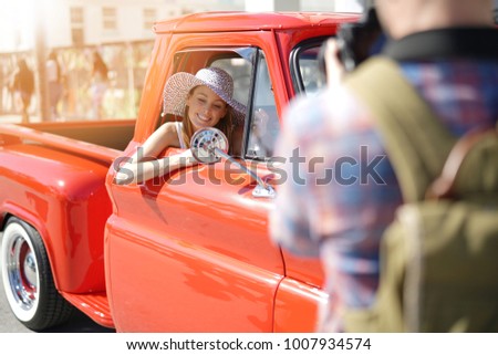 Photographer taking pictures of model sitting in old fashioned pick-up