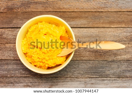 rice porridge from pumpkin with milk and wooden spoon on wooden retro grunge background top view close-up