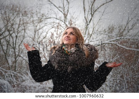 Beautiful happy smiling woman in winter outdoors. In the street snowfall. The girl lifted her hands up.