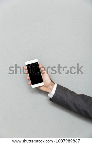 Cropped photo of male hand holding smartphone with blank screen isolated over gray background copy space