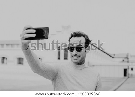 
handsome young man using his mobile phone, taking pictures with happy face outdoors on a sunny autumn day. Lifestyle.