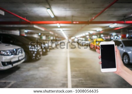 Hand holding mobile phone with blurred image of indoor car parking lot area, Internet, Social media