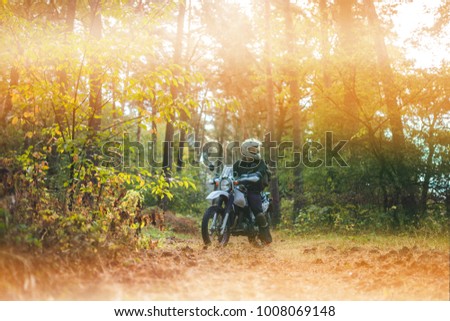 Man in dual sport helmet with backpack, enduro off road motorcycle on the forest road during sunrise. travel freedom concept, space for text, glow, blur